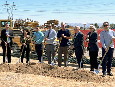 Staff from National Graphic Islamic Bank and from the Federal Home Loan Bank stand on a gravel pit with shovels with other community professionals in suits.